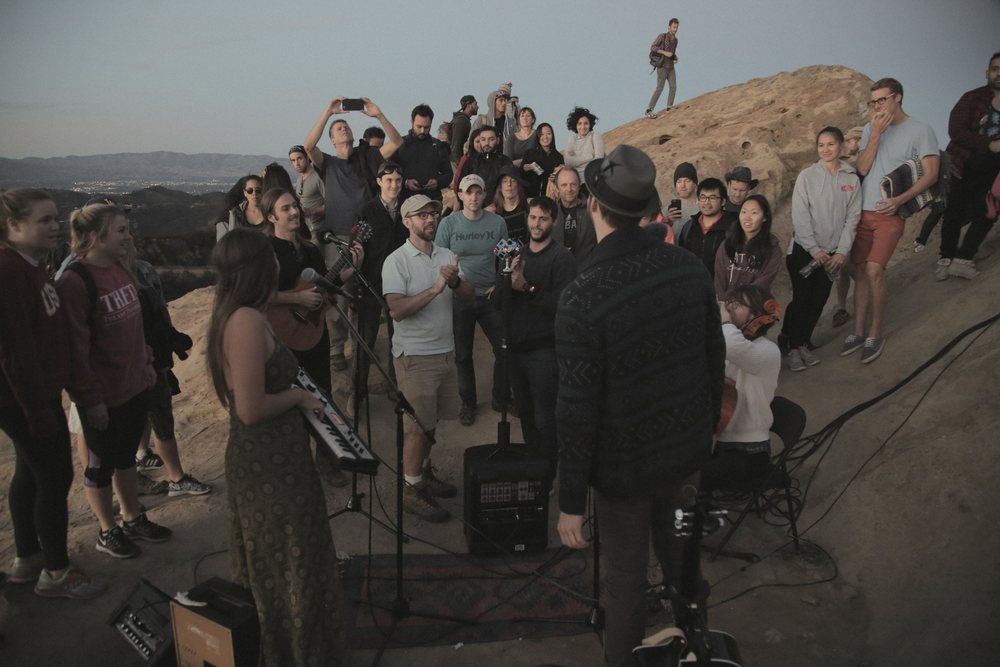A crowd gathered around musicians on the sandstone at Eagle Rock at dusk
