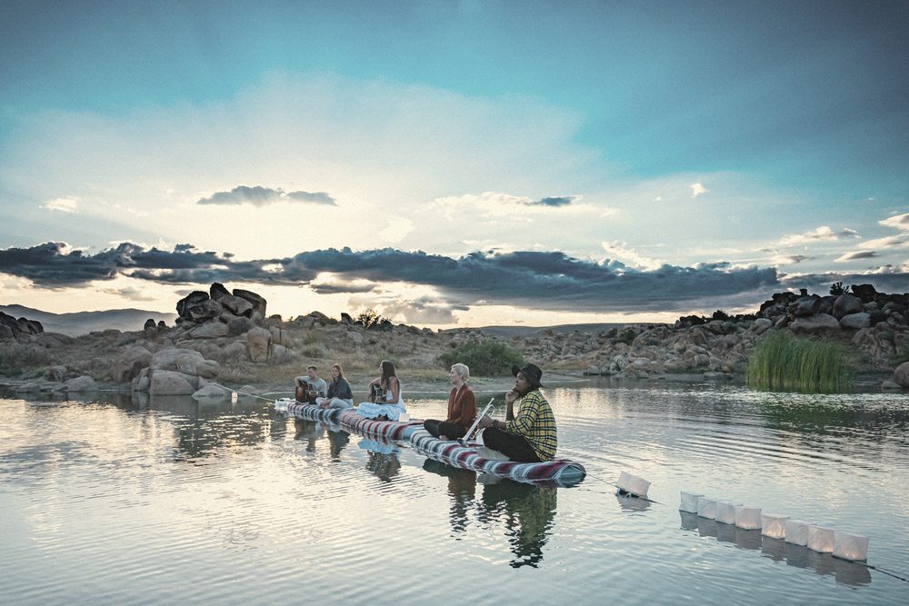 Musicians on a raft on a desert lake, lanterns floating beside them