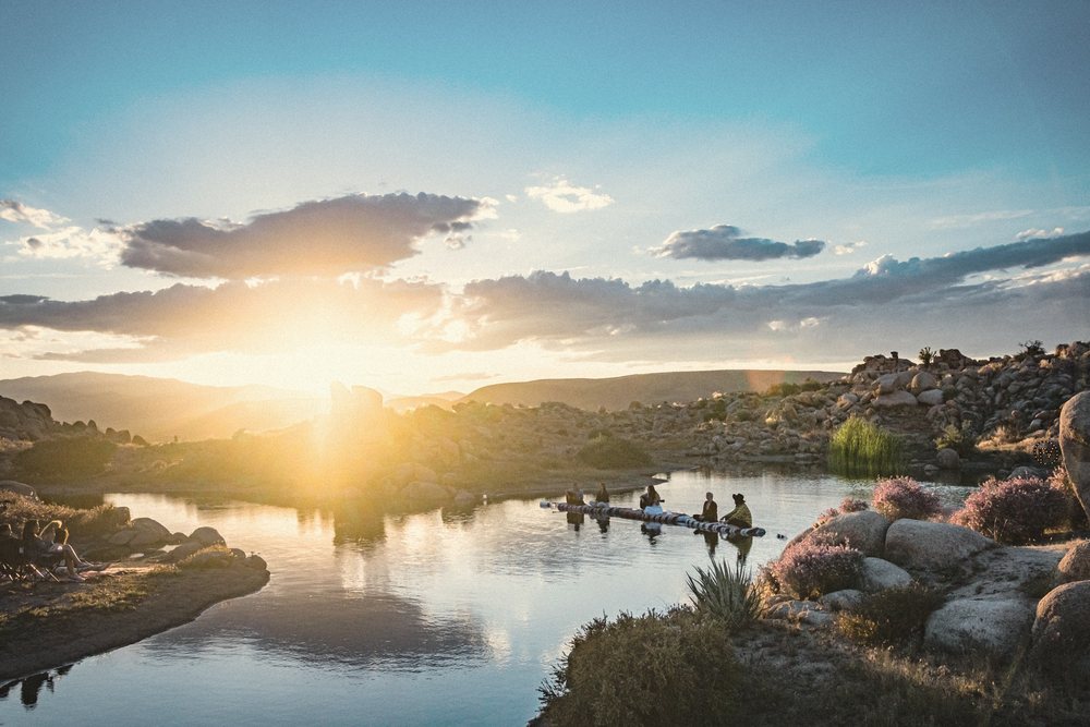 The sun setting over a desert lake at Joshua Tree, musicians playing on a raft on the water