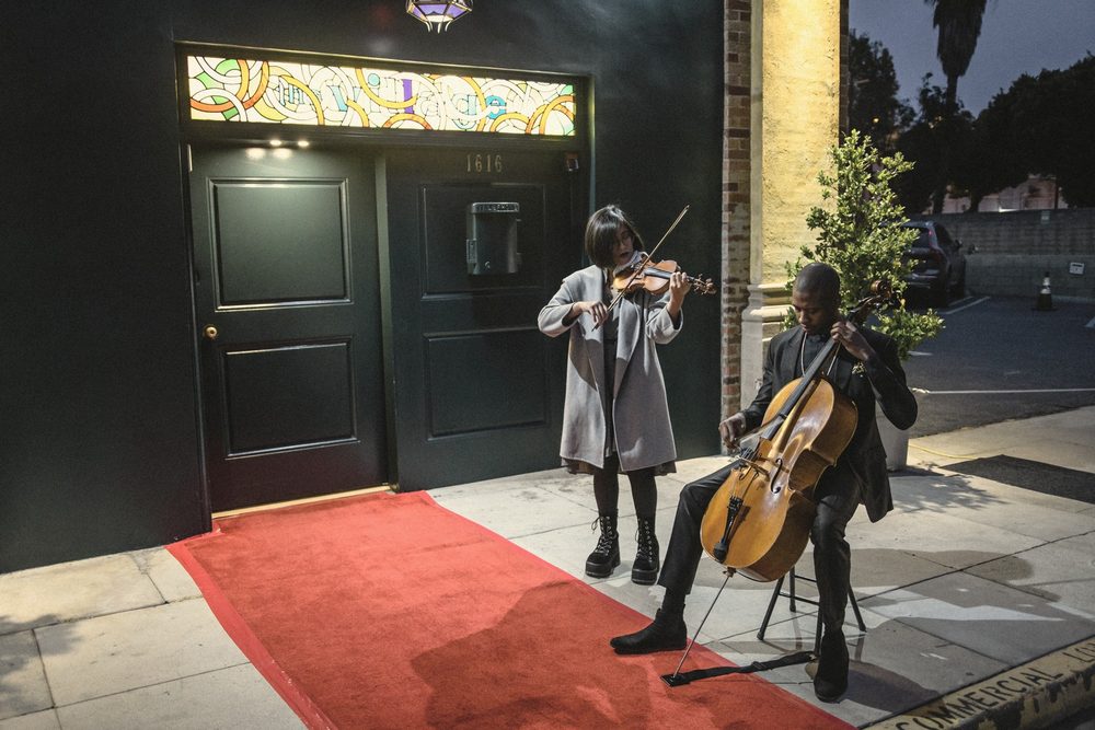 A violinist and a cellist playing on a red carpet at a doorway