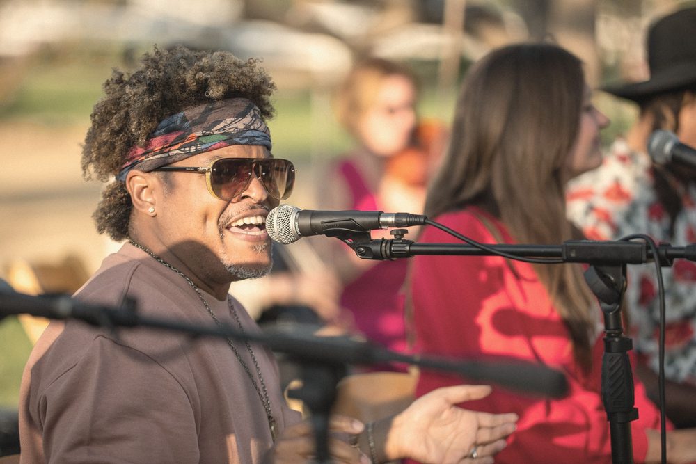 A singer in sunglasses and a headscarf laughing at the microphone