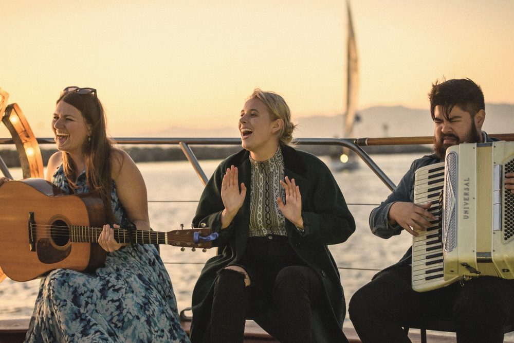 A singer, a guitarist and an accordion player on the deck of a boat at sunset